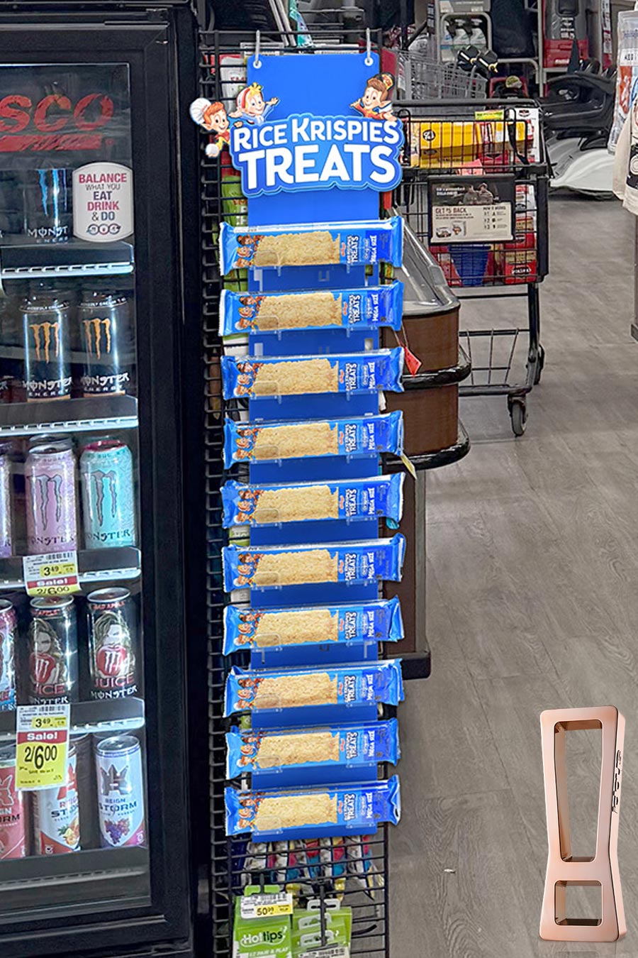 Display rack of Rice Krispies Treats bars in blue packaging beside a beverage fridge in a store aisle.